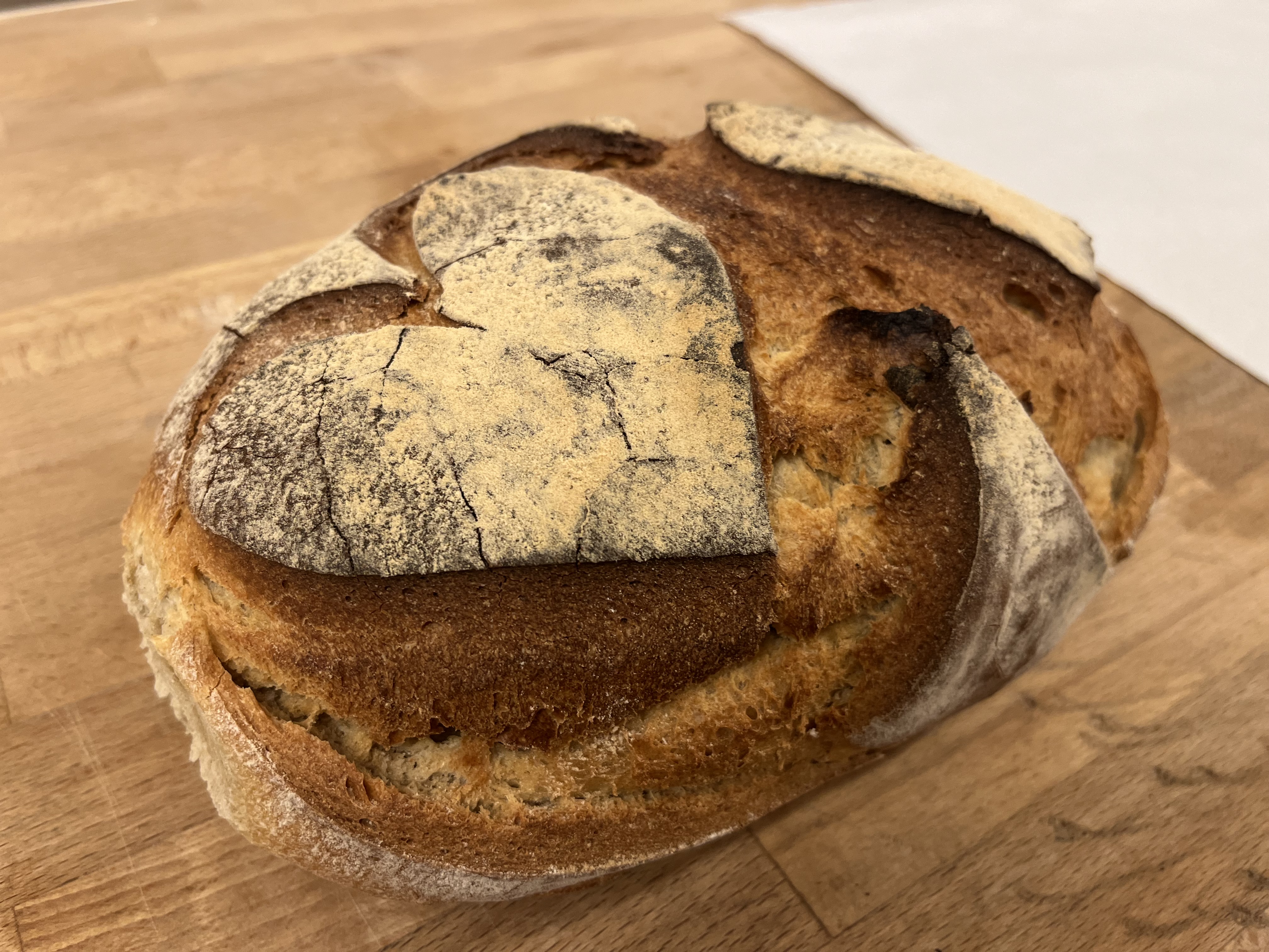 Frisch gebackener Laib mit dunkel gerissener Kruste auf einer Holzplatte
